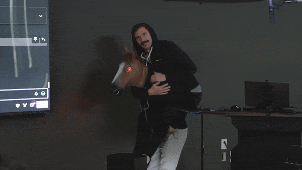 Man in a black hoodie embracing a person wearing a horse head mask with red glowing eyes in a conference room.
